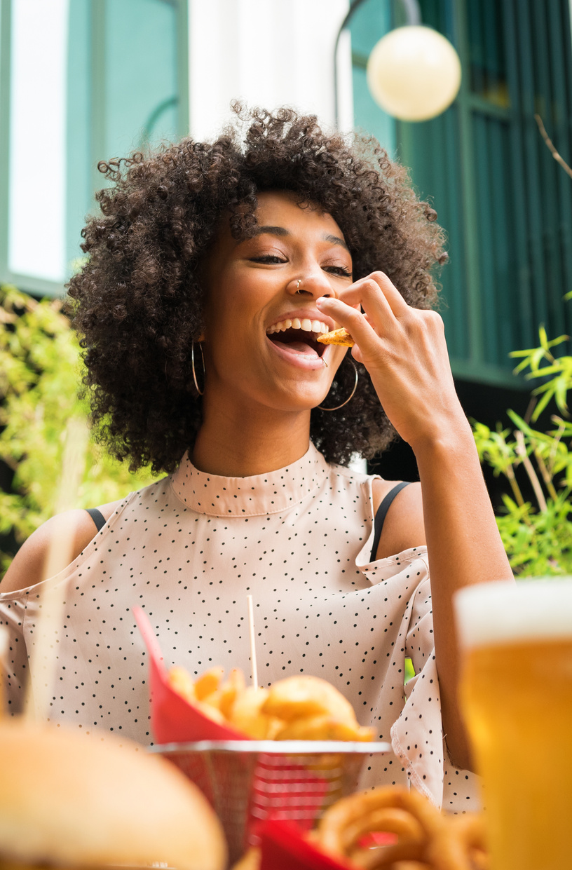 Smiling happy Black woman eating potato wedges in a pub